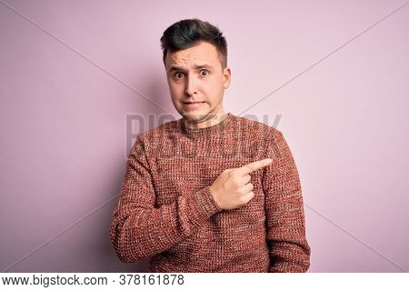 Young handsome caucasian man wearing casual winter sweater over pink isolated background Pointing aside worried and nervous with forefinger, concerned and surprised expression