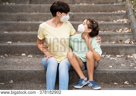 Middle-aged Mother And Daughter Sit On The Street Wearing Masks
