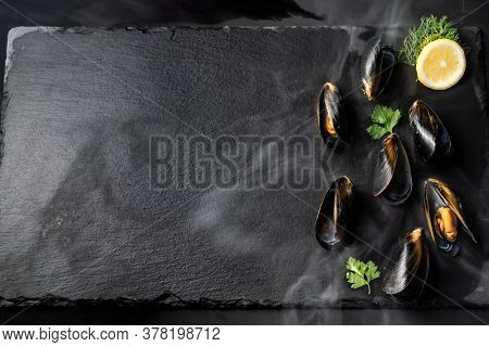 Black mussel with lemon serve on black stone plate. Fresh seafood food and european cuisine gourmet concept.