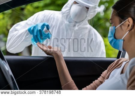 Medical staff give alcohol gel hand sanitiser to asian woman before coronavirus covid-19 test at drive thru station in hospital. New normal healthcare drive thru service and medical concept.