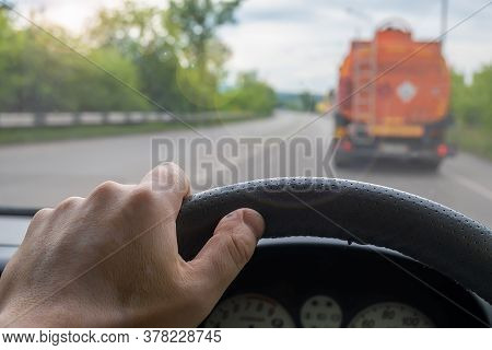 View Of The Driver Hand At The Wheel Of A Car That Is Driving Behind A Fuel Truck On The Road