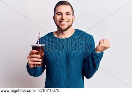 Young handsome man dirnking cola refreshment beverage screaming proud, celebrating victory and success very excited with raised arm 