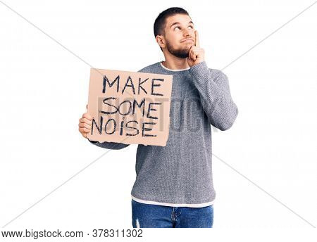 Young handsome man holding make some noise banner serious face thinking about question with hand on chin, thoughtful about confusing idea 