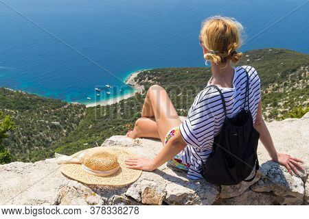 Active Sporty Woman On Summer Vacations Sitting On Old Stone Wall At Lubenice Village, Wearing Straw