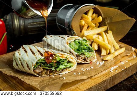 Shawarma Greens And Meat Drenched In The Sauce On A Wooden Board With Fries