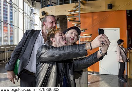 Kiev, Ukraine, 03.23.2020: Selfies Are Made By Two Men And A Girl. The Couple Sticks Out Their Tongu