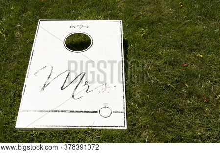 A White Cornhole Game On A Green Lawn With Mrs Written In Black As A Wedding Present.