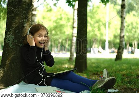 Happy Girl In White Headphones Using Digital Tablet Pc In The Park. Distant Learning Concept. Resili
