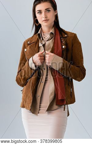Confident, Stylish Girl Touching Suede Jacket While Looking At Camera Isolated On Grey