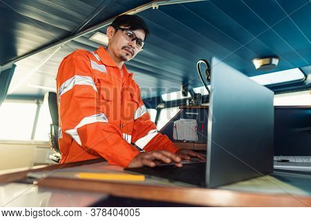 Filipino Deck Officer On Bridge Of Vessel Or Ship. He Is Using Laptop, Electronic Paperwork At Sea