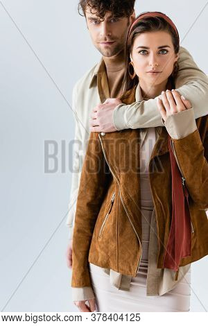Handsome Man Hugging Stylish Woman In Suede Jacket Isolated On Grey