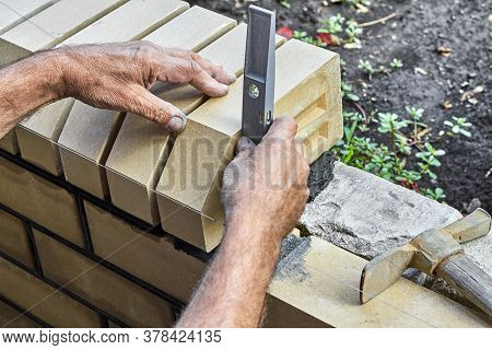 Bricklayer Levelling Bricks On The New Fence From Facing Bricks Using Building Level.