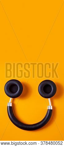 a pair of black wireless full size headphones upside down on an orange background, resembling a smiley face, in a vertical format to use for mobile stories or as smartphone wallpaper