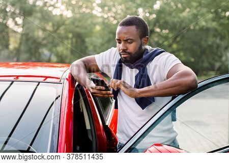 Concentrated Young African Man Using His Smart Phone To Check The Status Or Control His Car Insuranc