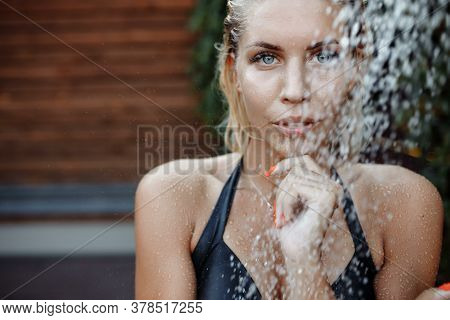 Shooting In The Aquazone With Falling Water Drops. A Girl With Blond Hair In A Black Swimsuit Under 