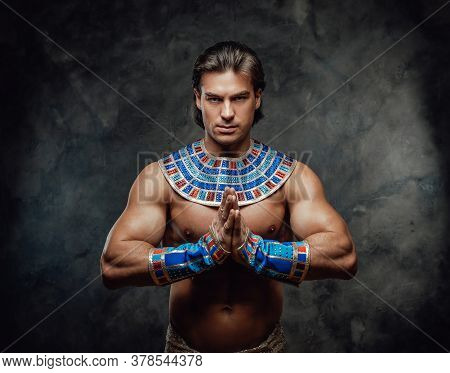 Athletic Man In Ancient Egyptian Costume Posing In The Studio With His Palms In The Sign Of Prayer