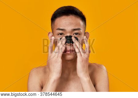 Look Well. Portrait Of Shirtless Young Asian Man Applying Charcoal Carbon Face Mask On His Nose Isol