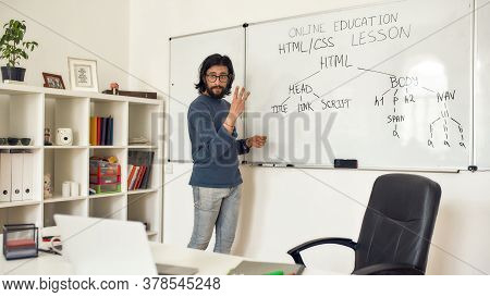 Teaching Code Programming. Young Bearded Male Teacher Pointing At Whiteboard And Explaining How To C