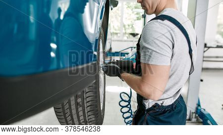Cropped Shot Of Male Mechanic Screwing Or Unscrewing Car Wheel Of Lifted Automobile By Pneumatic Wre