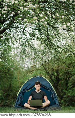 Man Working On Laptop In Tent In Nature. Young Freelancer Sitting In Camp. Relaxing In Camping Site 