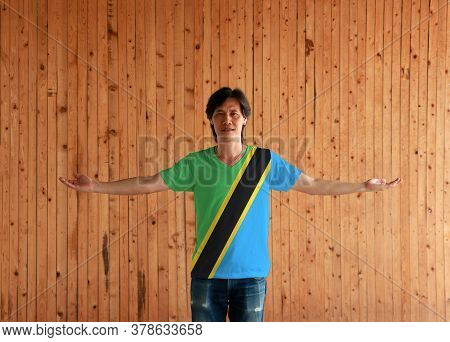 Man Wearing Tanzania Flag Color Shirt And Standing With Arms Wide Open On The Wooden Wall Background