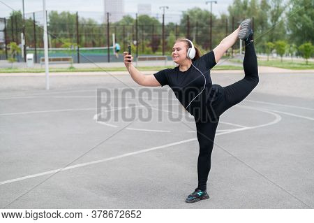 Beautiful Fat Young Woman In Headphones Makes A Figure Skater And Takes A Selfie. A Chubby Smiling G