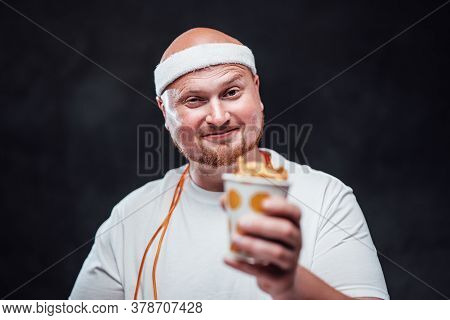 Plump Smiling Man In A White Duffle, Eating French Fries With Sauce, Standing On The Dark Background