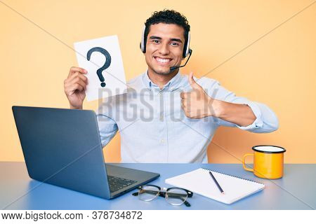 Young handsome hispanic man holding question mark as customer support smiling happy and positive, thumb up doing excellent and approval sign 