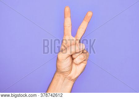 Hand of caucasian young man showing fingers over isolated purple background counting number 2 showing two fingers, gesturing victory and winner symbol