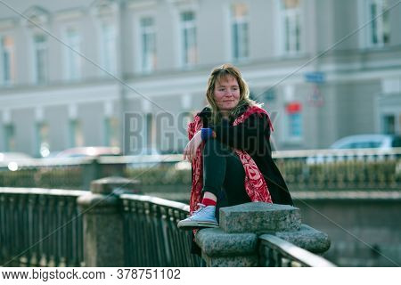 A young girl sits on the railing of the Griboedov canal embankment in Saint Petersburg.