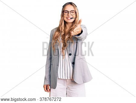 Young beautiful blonde woman wearing call center agent headset smiling friendly offering handshake as greeting and welcoming. successful business. 