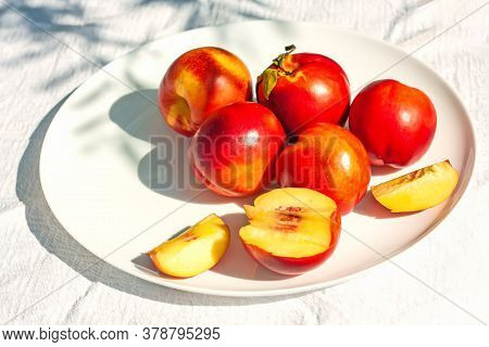 Red Ripe Organic Nectarine Fruits On The White Plate On Nature Background. Summertime Healthy Eating