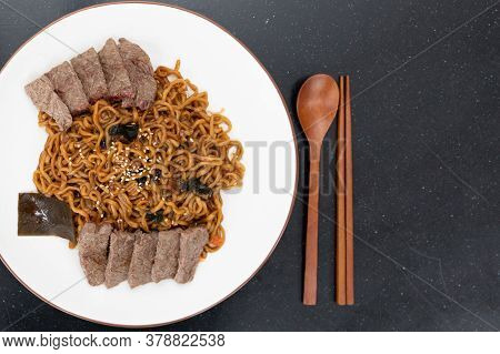 Top View Image Of Korean Black Bean Noodles Served With Sliced Meat With Wooden Eating Utensils.