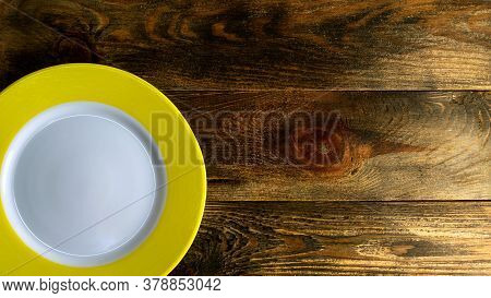 Empty Round Ceramic Plate With Yellow Edge On Rough Wooden Background Or Table. Copy Space For Text.