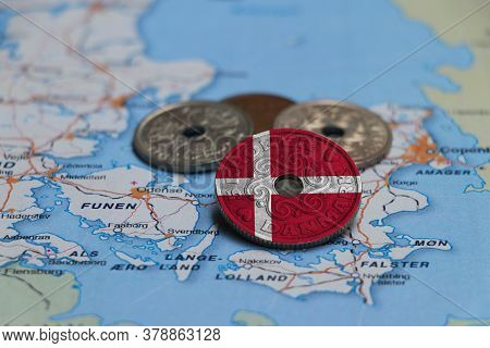 Denmark Flag On The Coin With Heap Of Danish Kroner Money On The Map. Concept Of Finance Or Currency