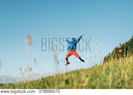 Backpacker Traveler Emotionally Jumping Over Green Grass Mountain Meadow With Backpack With Wide Ope