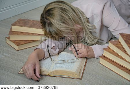 Young Blonde Woman Is Surrounded By Books Had Fallen Asleep On The Floor While Studying. Glasses On 