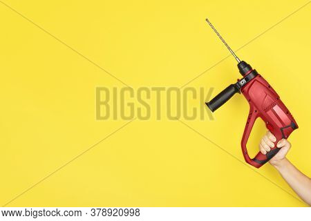 Red Puncher In The Hands Of A Builder. Female Hand Hold New Puncher Or Drill Isolated On Yellow Back