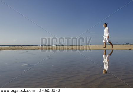 Man With Medical Mask Sitting On Beach During Coronavirus Covid 19 Pandemic, Social Distance Concept