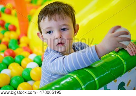 Toddler Baby Plays In The Pool With Balls. Child Boy Crawling In The Pool With Plastic Balls. Kid Ag
