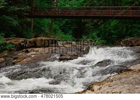 River Creek And Wooden Bridge In Lacamas Regional Park, Washington, Usa. Cascade Falls Over Mossy Ro