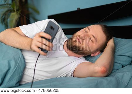 Caucasian Man Texting On Cellphone And Browsing Internet Lying In Ded In Bedroom Indoors. Guy Uses M