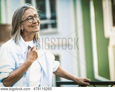 Happiness In Old Age, Mature Woman With Radiant Smile Standing On Balcony Overlooking Old Street In 