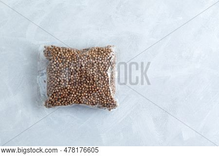 Dried Coriander Seeds In Clear Plastic Bag On Grey Textured Background. Top View, Copy Space.