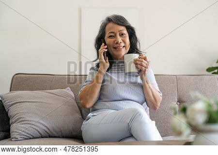 Cheerful Happy Aged Woman Talking On Cellphone At Table With Coffice, Using Wireless Online Connecti