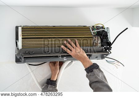 Hands Of Man Technician In Uniform Installing Air Conditioner In Apartment On Wall. Maintenance And 