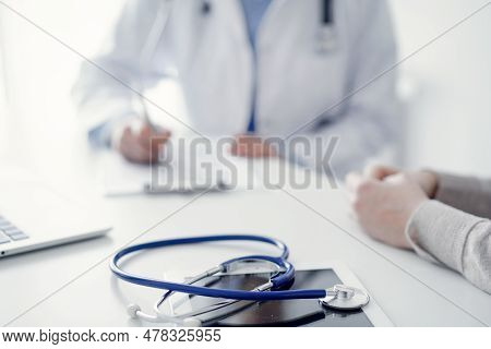 Stethoscope Lying On The Tablet Computer In Front Of A Doctor And Patient At The Background . Medici