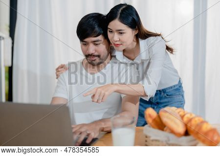 Happy Young Loving Family Couple Looking At Laptop Computer Screen, Reading Ecipes. Wife Showing Emb