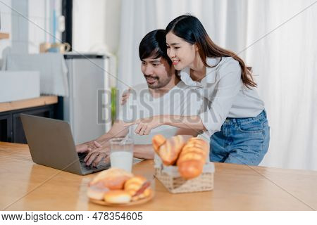 Happy Young Loving Family Couple Looking At Laptop Computer Screen, Reading Ecipes. Wife Showing Emb