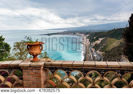 Mediterranean Flowering Plant In A Stone Ceramic Pot With Scenic View On Seaside And Mount Etna Volc